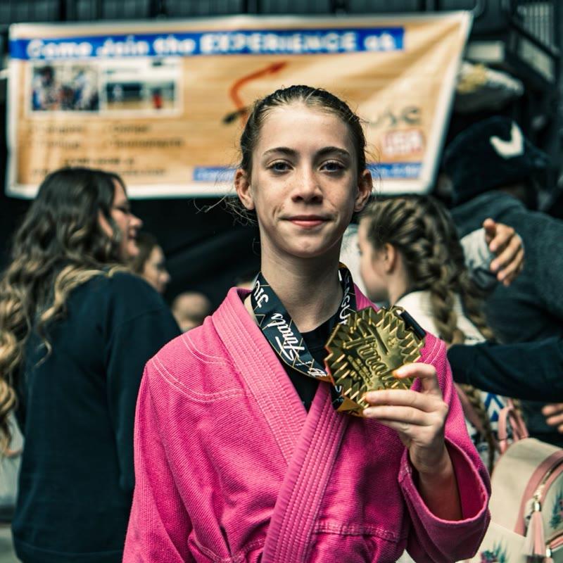 Young athlete in a pink gi with a JJWL Finals gold medal